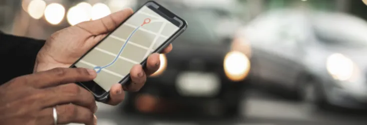 Main tenant un smartphone affichant un itinéraire, taxi en arrière-plan